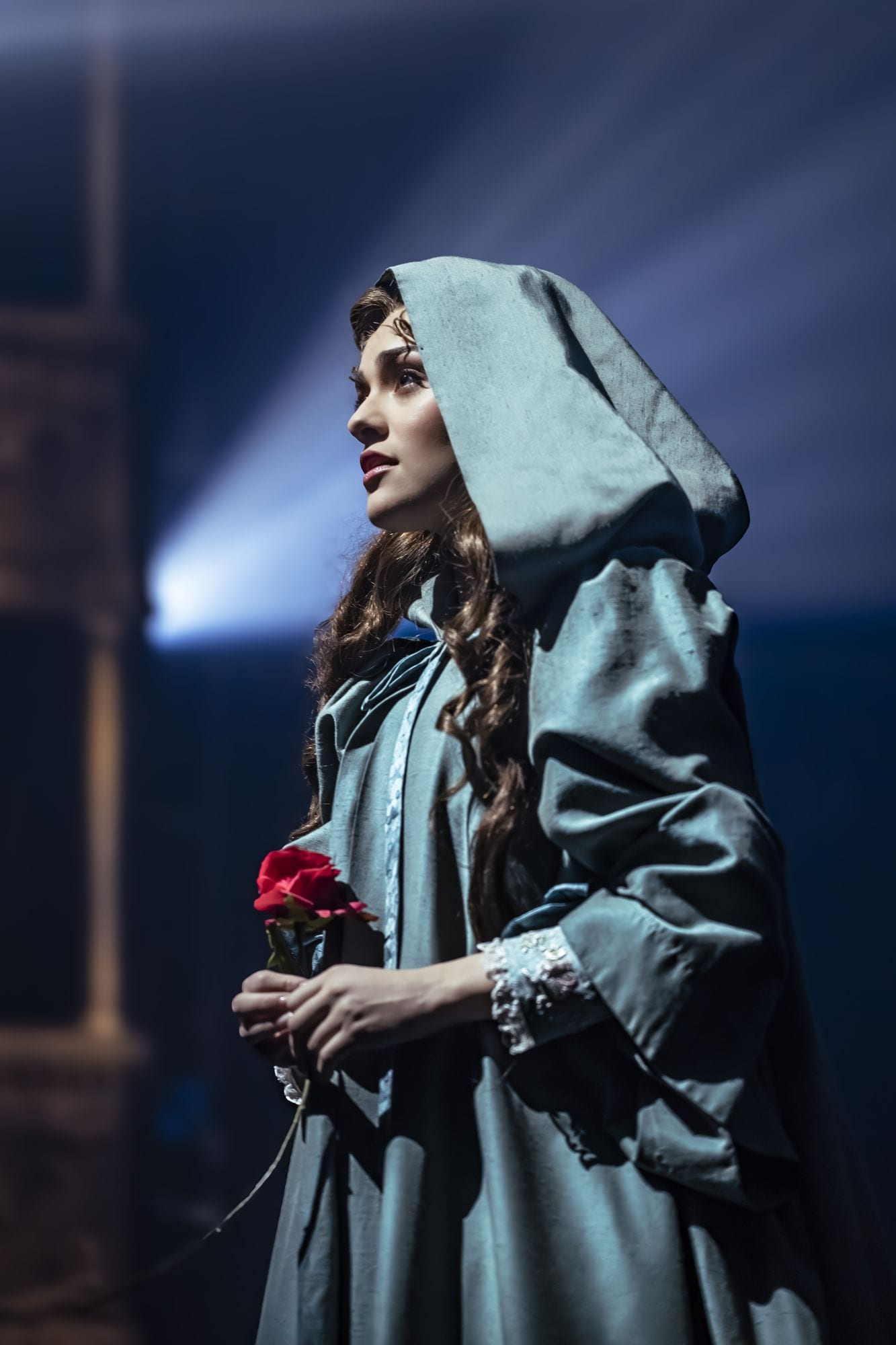 Christine Daaé con capa y capucha, sosteniendo una rosa roja