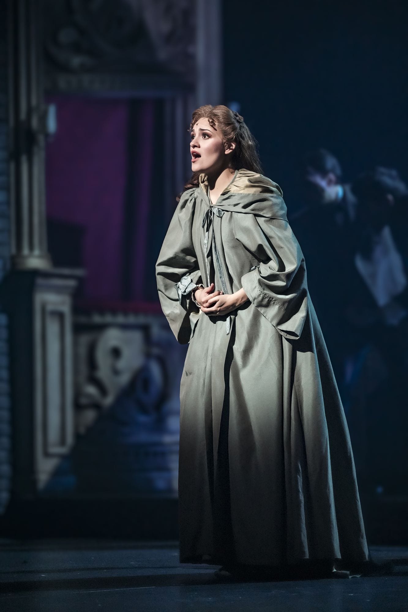 Christine Daaé con vestido gris de viaje, rodeada por el elenco