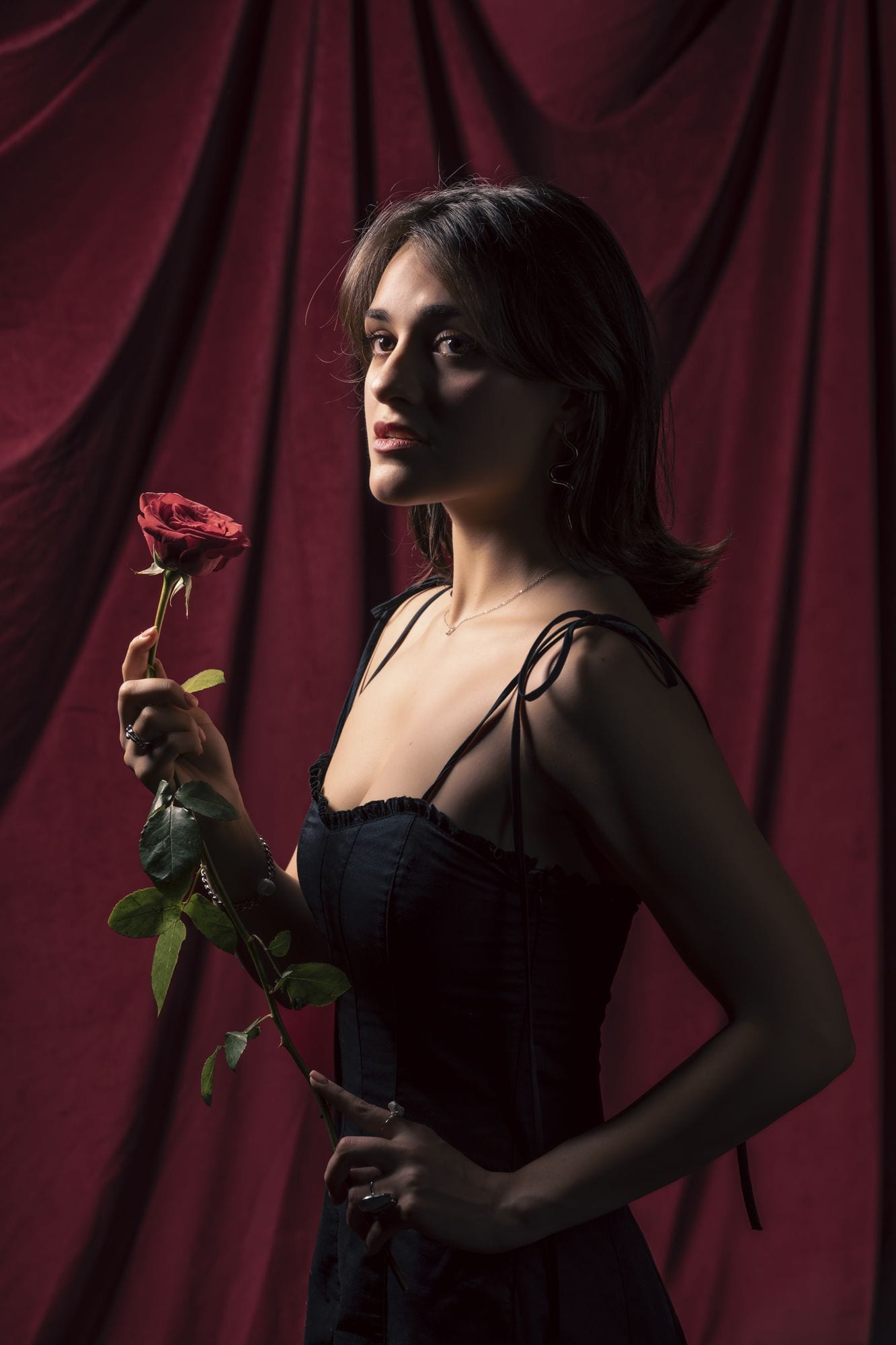 De pie con una rosa roja frente a una cortina carmesí