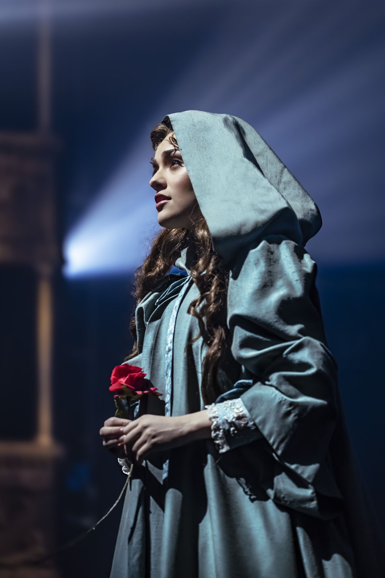 Christine Daaé in a hooded cloak holding a single red rose