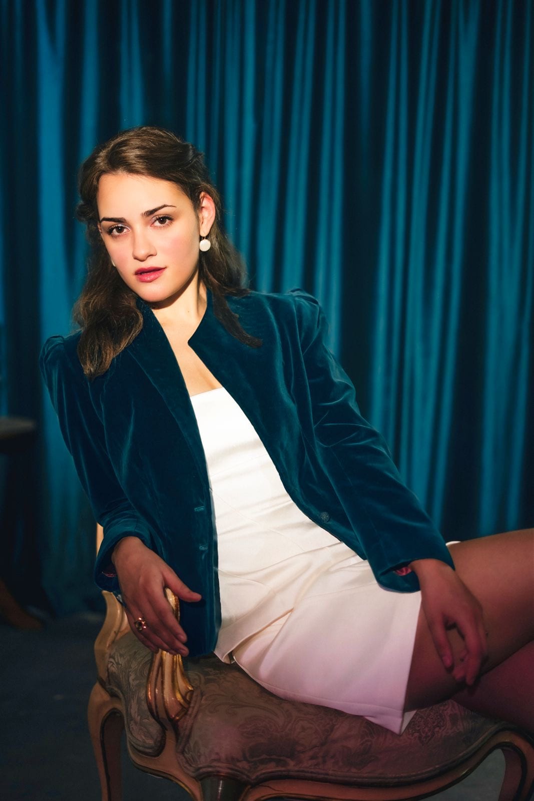 Seated against a teal velvet curtain